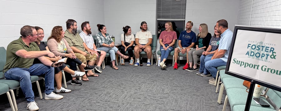Members of the Rich Fork Church foster and adopt support group laughing together in a circle beside their support group sign